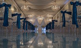 A wedding ceremony set up with blue accents on the chairs and chandeliers hanging from the ceiling