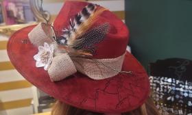 A red hat with mountain drawing accents, feathers, and ribbon tied around it
