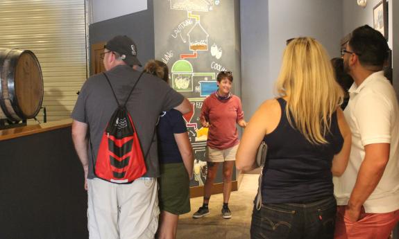 A group of tour guests surround a tour guide at a local brew pub