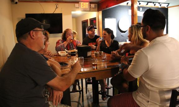 A tour group sits around a high top with trying samples of beer