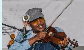 Jerron Paxton, blues performer, playing his fiddle and singing while smiling