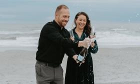 A couple opening a champagne bottle at the beach