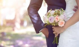 A bride and groom holding hands, the bride's bouquet is in focus with soft pink and peach flowers
