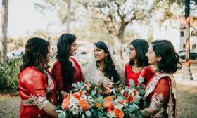 A group of four bridesmaids dressed in red and gold attire, smiling with the bride