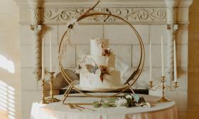 A table featuring a wedding cake decorated with natural elements, set against a circular gold backdrop
