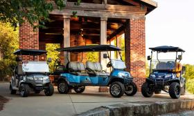 Three golf carts built for travel on city streets arrayed in front of a brick pavillion