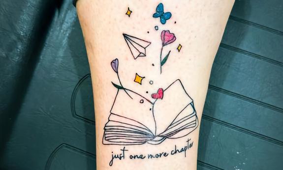 A tattoo featuring an open book with various objects and lettering