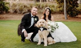 A bride, groom, and their dog, dressed up for the wedding, sitting on the lawn at TPC Sawgrass with the clubhouse behind them