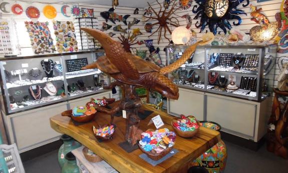 A wooden carving of a sea turtle with glass jewelry displays behind