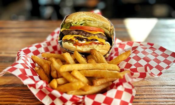 A cheeseburger and fries, nestled in red and white gigham paper, in a basket