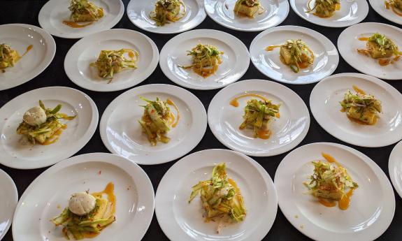 A table with a black cloth, covered with white plates of gourmet appetizers