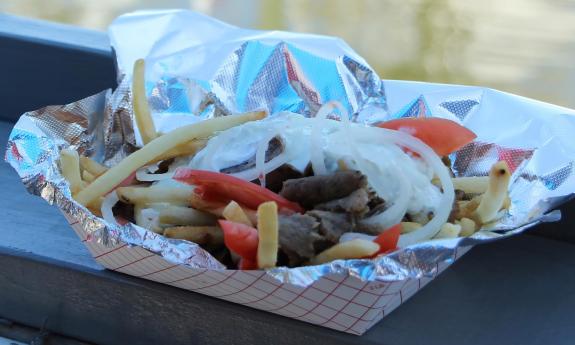 A tray of gyro fries — tomatoes, onions, and tzatziki sauce