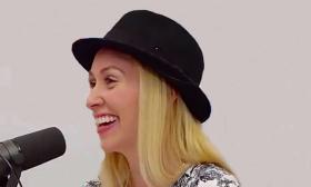 musician Kyra Livingston at the microphone, laughing, in black bowler hat