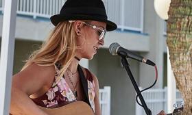 Musician Kyra Livingston playing guitar in front of microphone, in black bowler hat