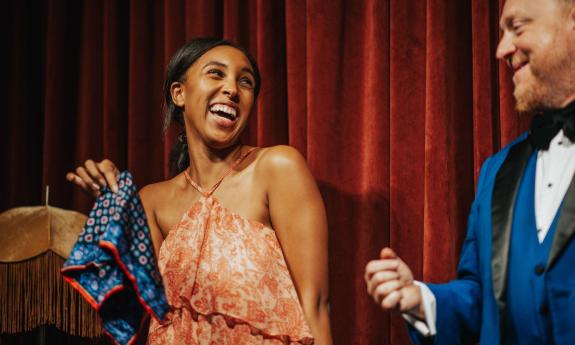 Master Magician Bill Abbott in a blue suit, interacts with an audience member who is holding his patterned silk hankerchief