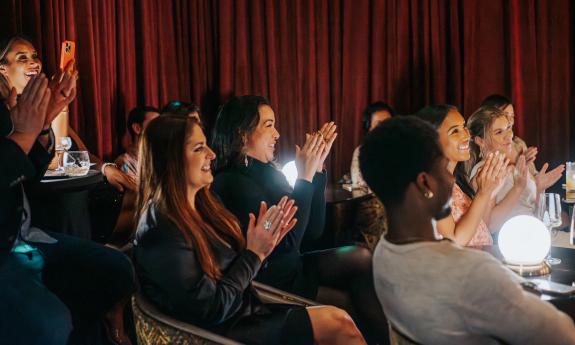 An audience in the intimate Magic Hideaway, applauding and smiling