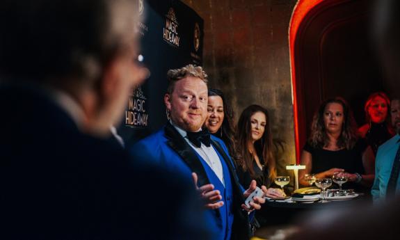 Master Magician Bill Abbott, in a blue tux, holds a deck of cards as he dazzles guests before the show