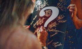A woman from the audience in a magic show, writing on a board that has a large question mark on it