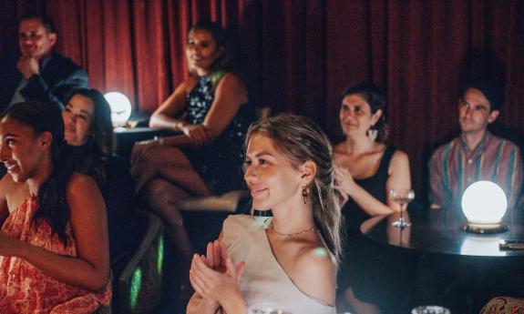 Audience members in a magic show, at tables lit by globe lamps