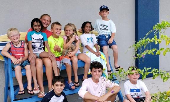 Young surf campers, seated on a blue bench with their instructor