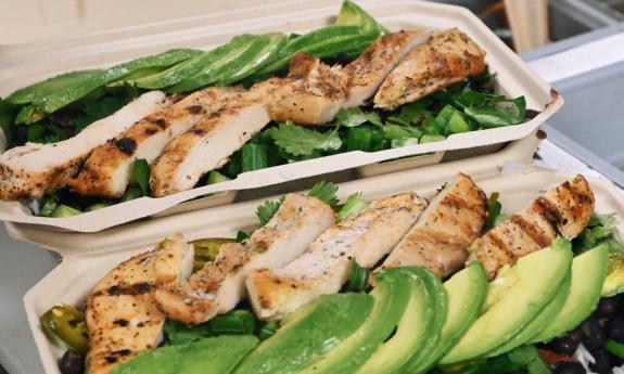 Close up of two to-go containers full of chicken, cilantro, avocadoes, and rice.