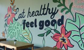 A mural with the text "Eat Healthy, Feel Good" surrounded in flowers and leaves backs the seating area of Crave 312.