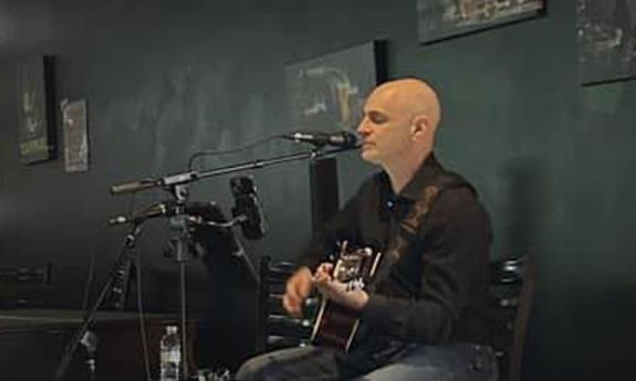 Kevin Mark playing guitar on stage, singing into microphone