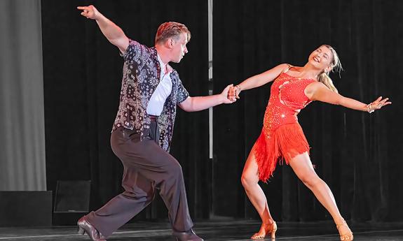 A couple dance on stage, holding hands, with their other arms flung out