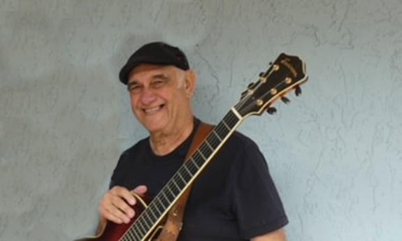 Guitarist Al Canali with his instrument, in front of a white wall.