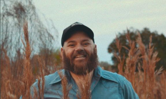 Musician Kirk Whalen in black ball cap, in wheat field, smiling