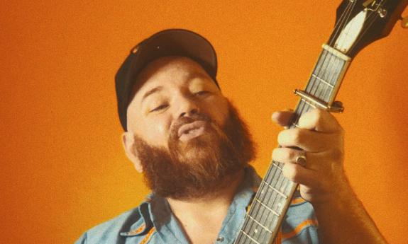 Musician Kirk Whalen holding stringed instrument, with orange background