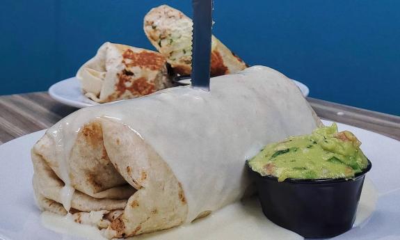 A burrito covered in queso and a side of guacamole