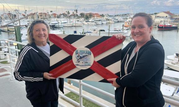 Two women holding a El Pescado Billfish Tournament flag sign