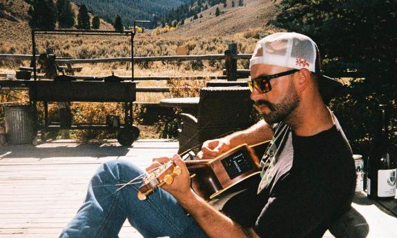 Oland Tucker playing his guitar on a deck in the Colorado Mountains