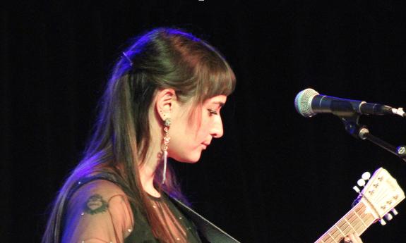Cristina Vane, on stage wearing black, with her cream-colored resonator guitar