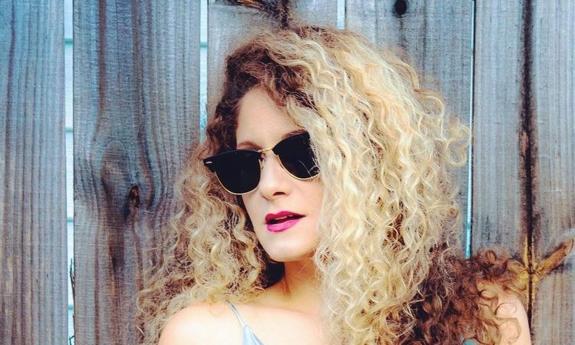 Singer/songwriter Rachael Warfield in sunglasses, outside, against a wooden fence