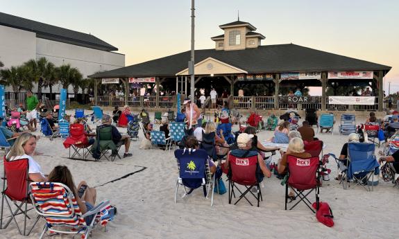People lounging on the sand enjoying live music