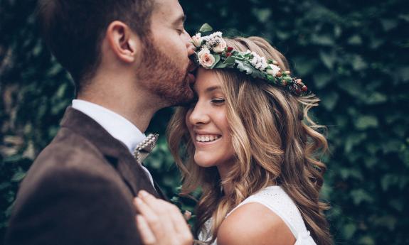 A couple hug as the groom kisses the bride's forehead 