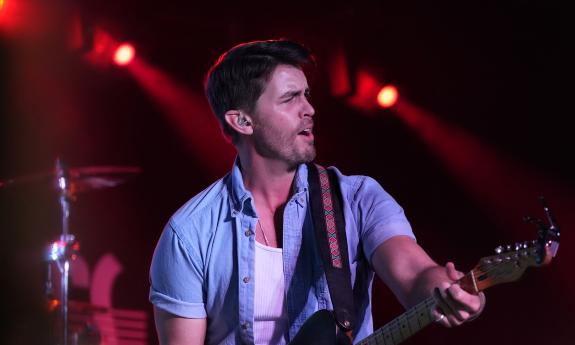 Dylan Gerard, a young country star, performing on stage with his guitar, and wearing a short-sleeved denim shirt