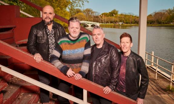 Bandmates from Barenaked Ladies pose on a staircase with a river as a backdrop. 