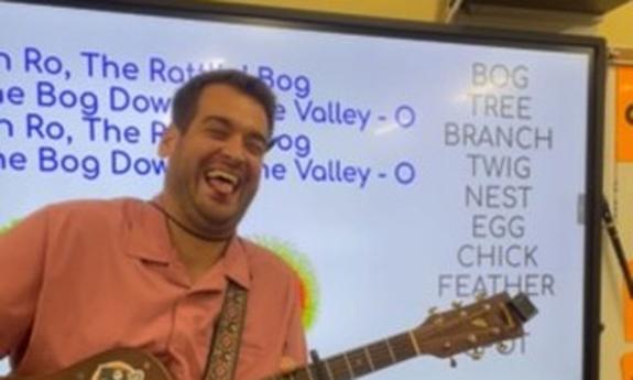 Jeremy Price playing guitar in a classroom, grinning