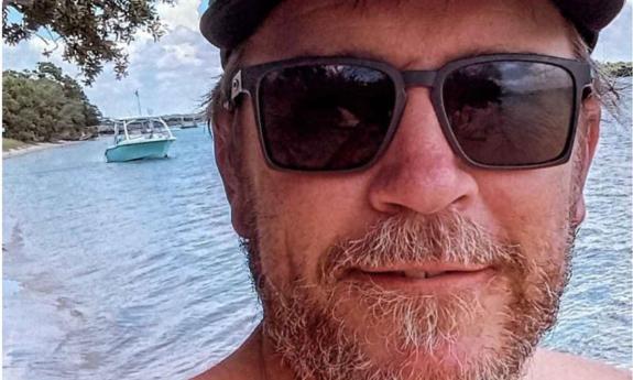 Singer songwriter Kevin Edwards grinning, outside at the water edge