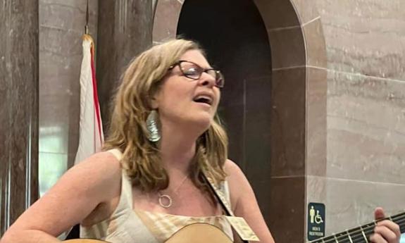 Musician Kim Blackburn playing her guitar and singing, outside.