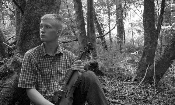 Ben Kiser holding a fiddle in the woods