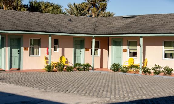 The motel, painted seashell pink with soft green doors has bright gold chairs at each unit