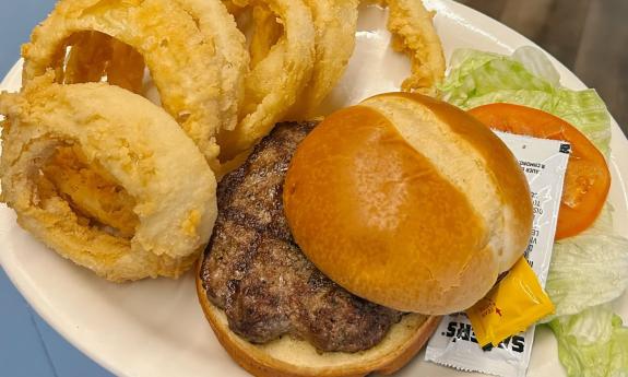 House-made onion rings with an Angus beef burger on a white plate