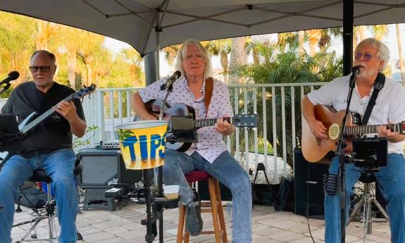 Three musicians, a bassist and two guitarists, under an awning on an outdoor stage