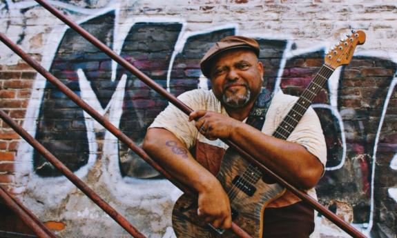 Kevin Burt clutches his guitar on a staircase with graffiti as a backdrop.