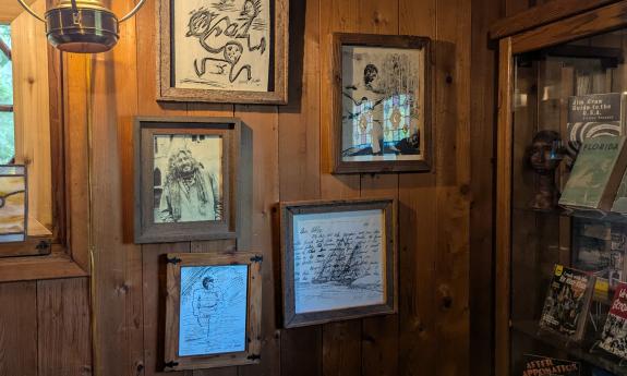 A wall of art and a bookcase, featuring work by artists who stayed at Beluthahatchee