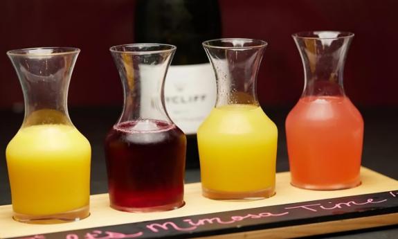 A mimosa flight, one bottle of sparkling wine served with four different juices